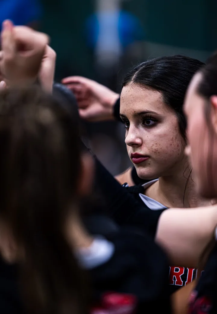 A volleyball player listens closely while surrounded by teammates in a huddle.