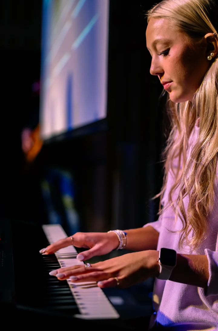 A young musician plays a keyboard under stage lighting.