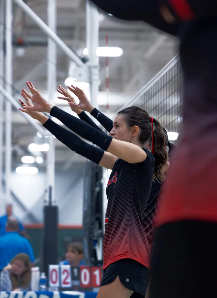 A volleyball player in red and black extends her arms near the sideline.