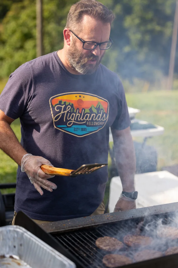 A man tends food on a smoking grill at an outdoor gathering.
