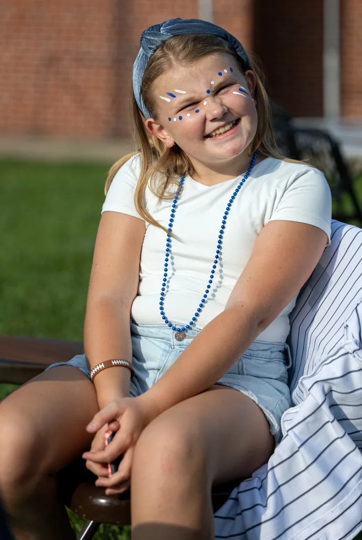 A smiling child sits outdoors beside a table at a community gathering.