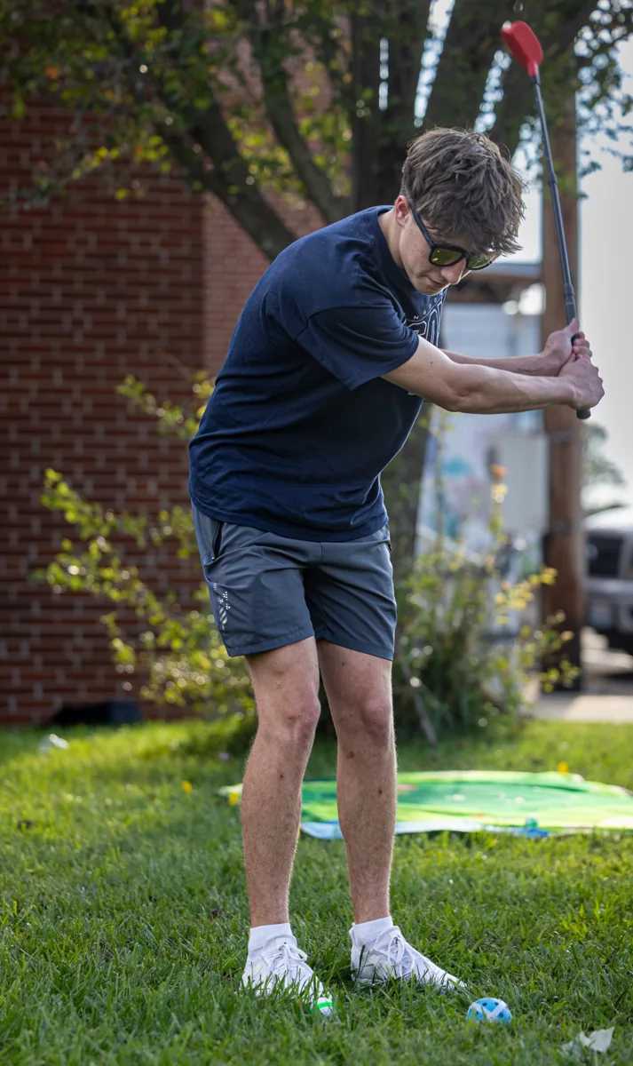 A young man leans forward to play an outdoor lawn game.
