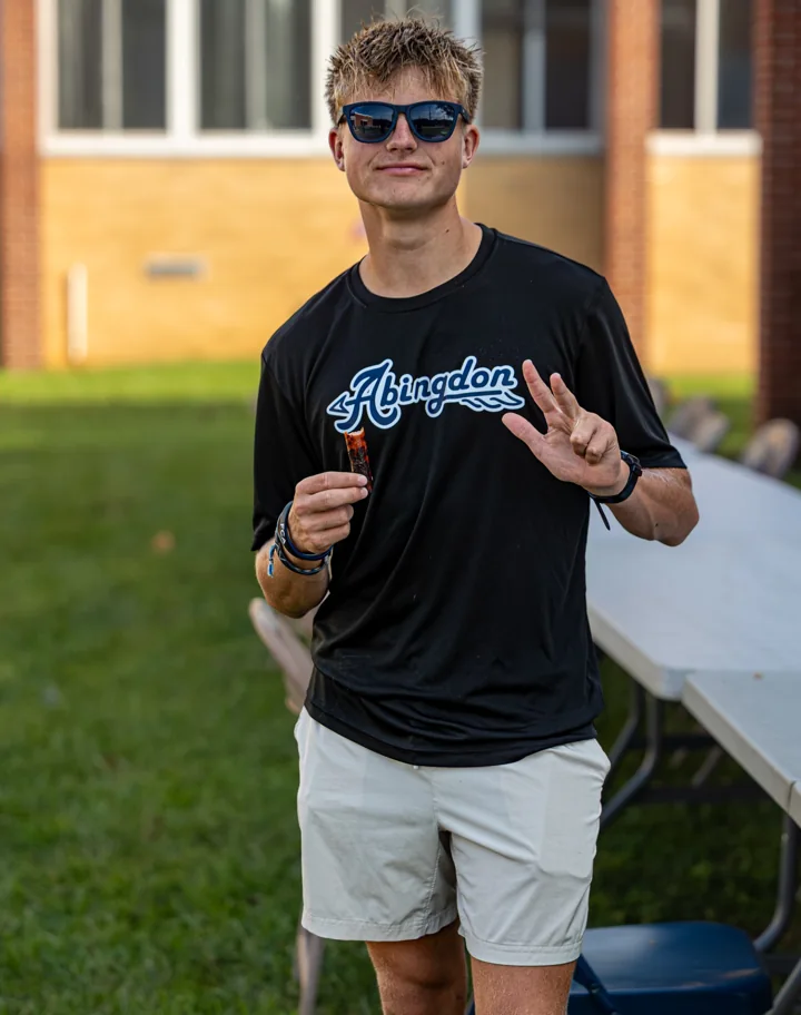 A young man in sunglasses stands outdoors at a community gathering.