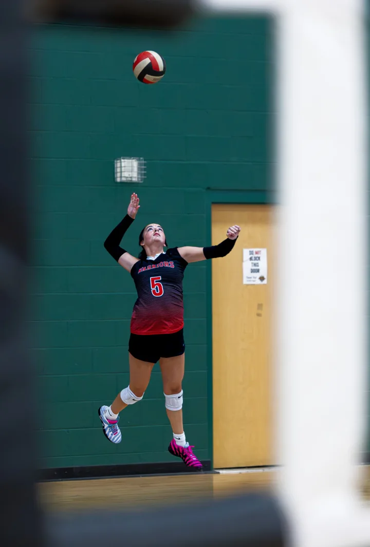 A volleyball player in red and black jumps to serve with the ball overhead.
