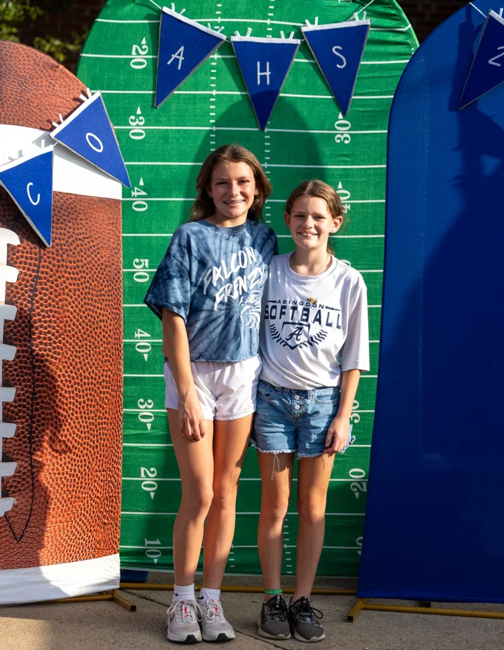 Two people pose together in front of a football-themed backdrop.