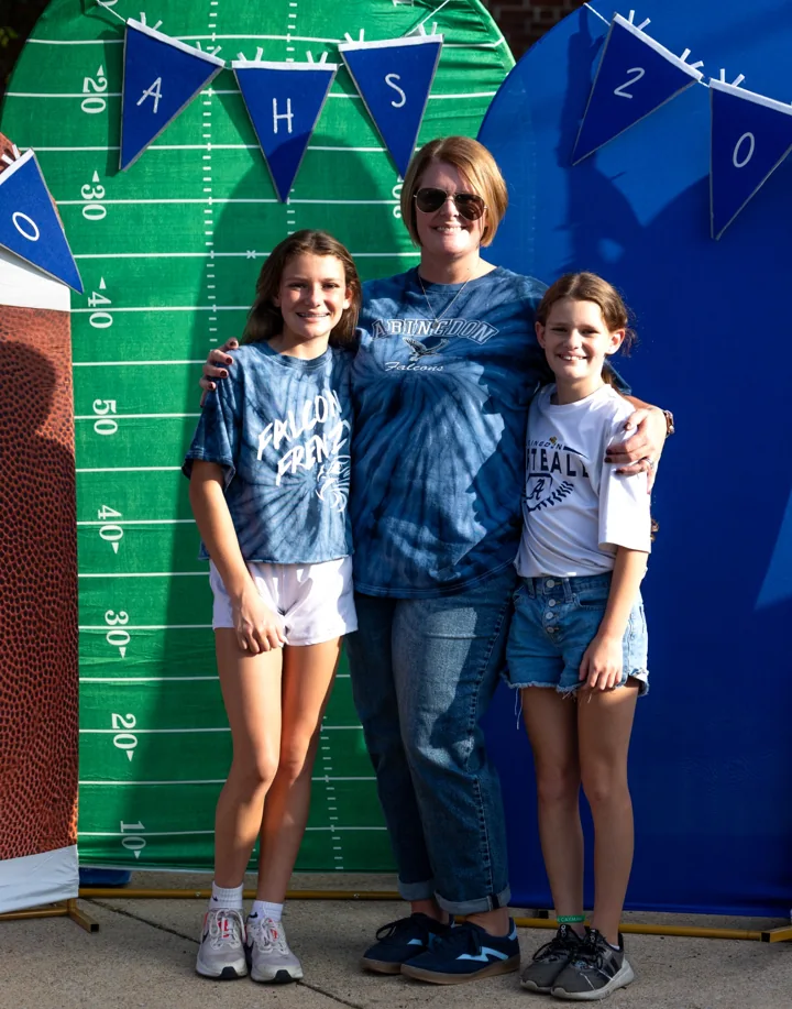 Three people pose together at a football-themed photo backdrop.