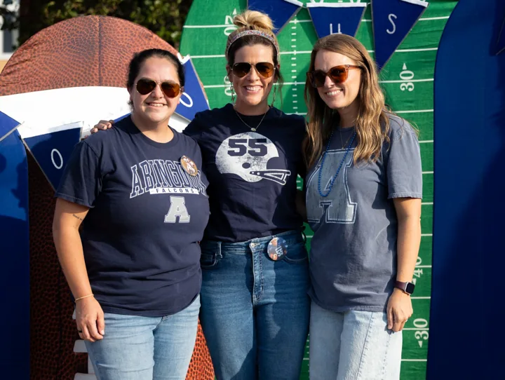Three people in team shirts pose together in front of a football-themed backdrop.