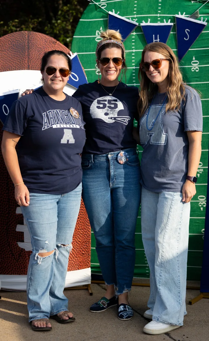 Three smiling people stand together at a football-themed photo backdrop.