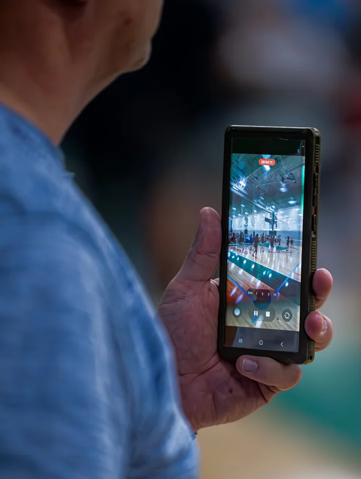 A spectator records a volleyball match on a phone from the stands.