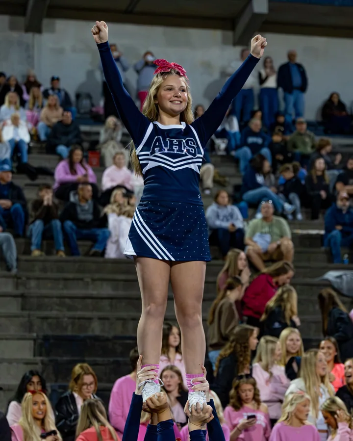 A smiling cheerleader holds her arms high while balanced above her teammates.