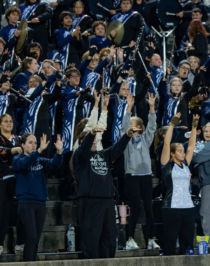 A marching band performs from the football stands under stadium lights.