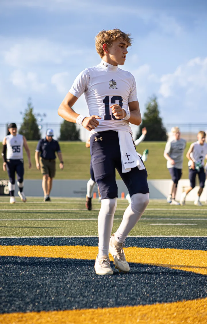 An athlete in a white number 18 warm-up shirt jogs across the field beneath blue sky.