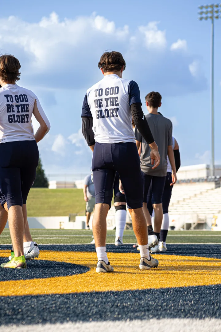 Football teammates in matching white warm-up shirts walk across the field.