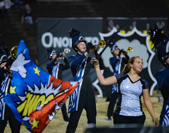 A marching musician performs beside a color guard flag during a night show.