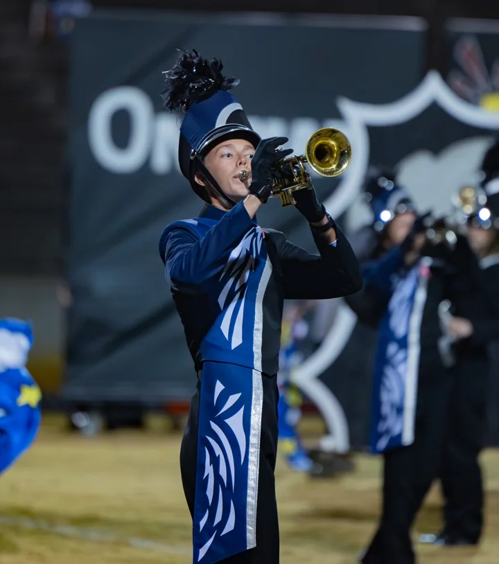 A marching musician raises a brass instrument during a halftime performance.