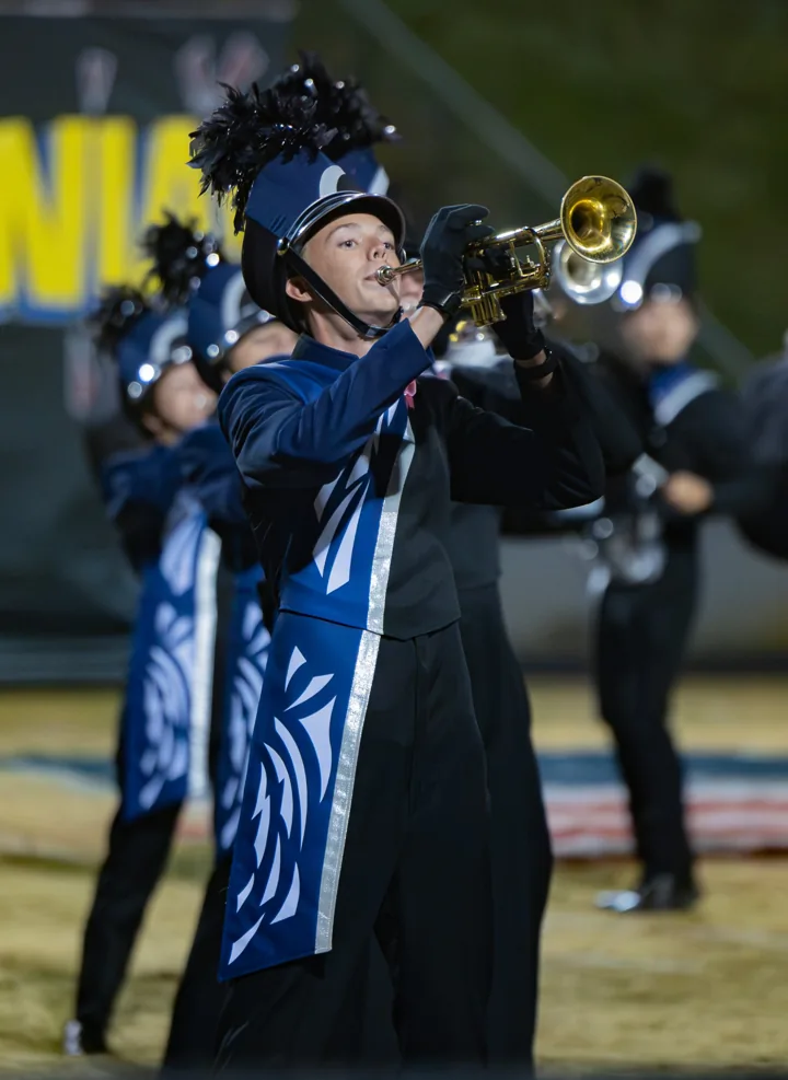 A marching musician plays a brass instrument under stadium lights.