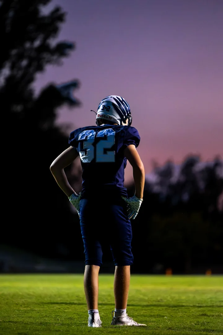 A football player stands alone on the field beneath a purple evening sky.